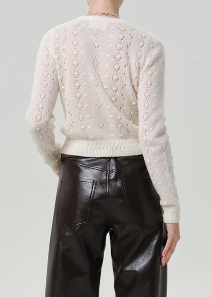 Woman wearing an ivory button-front cardigan with black leather pants viewed from the back on a grey background.