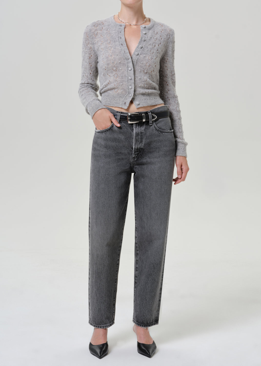 Woman wearing a grey button-front cardigan with dark grey jeans on a grey background.