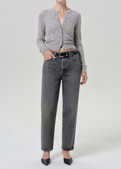 Woman wearing a grey button-front cardigan with dark grey jeans on a grey background.