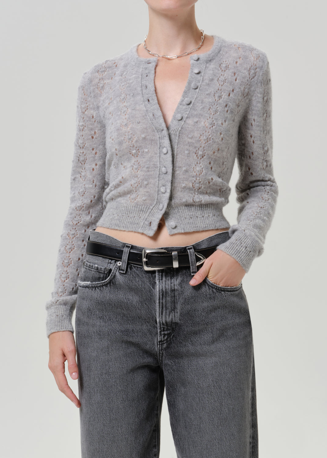 Woman wearing a grey button-front cardigan with dark grey jeans on a grey background.