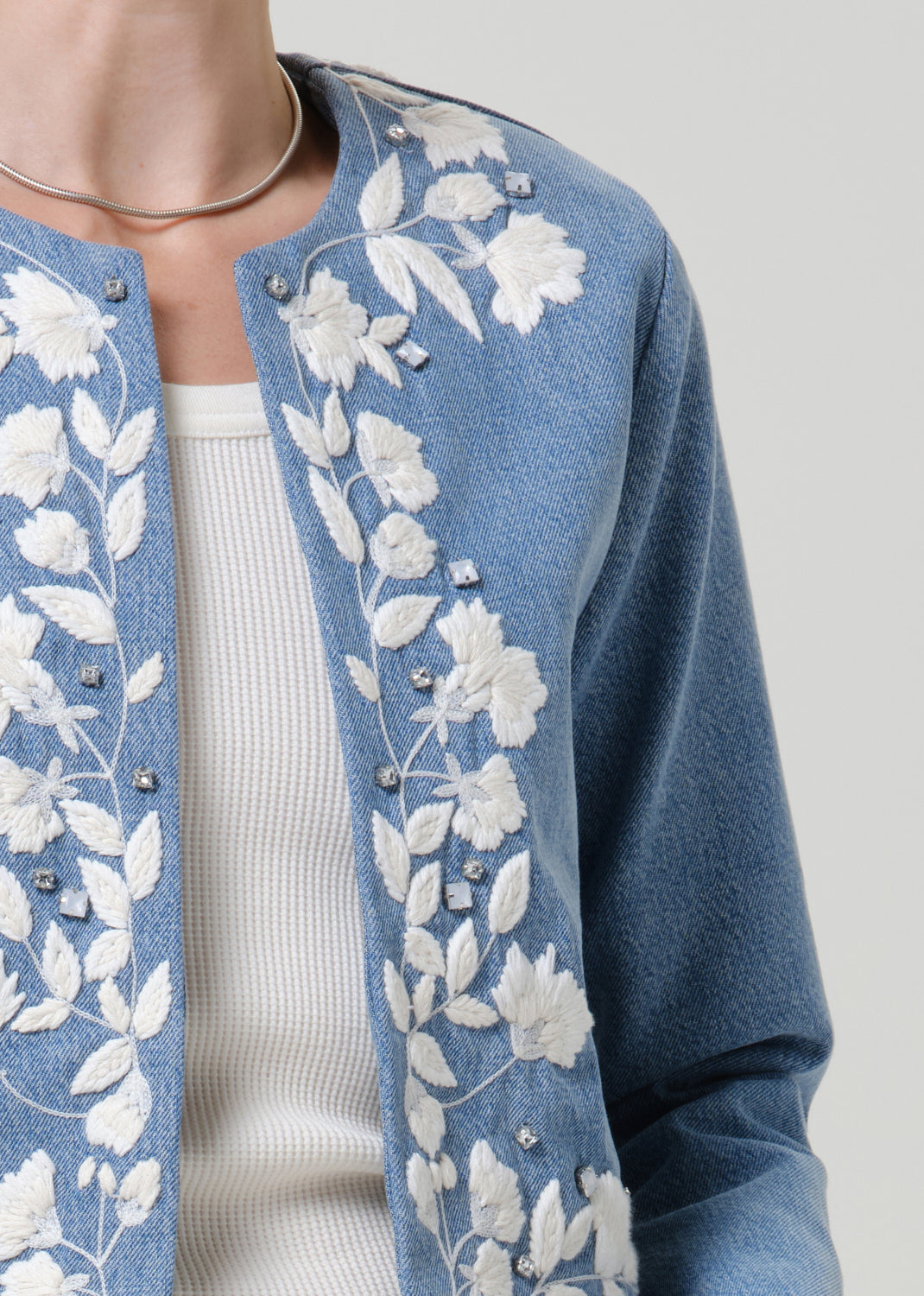 Close-up of a light blue floral denim jacket on a grey background.
