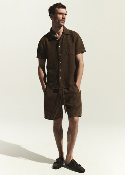 Man wearing a brown linen shirt with matching shorts standing against a white background