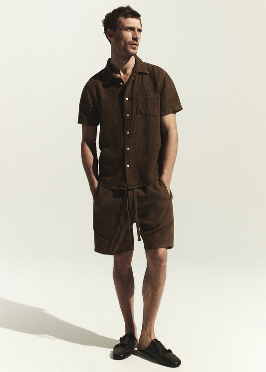 Man wearing a brown linen shirt with matching shorts standing against a white background