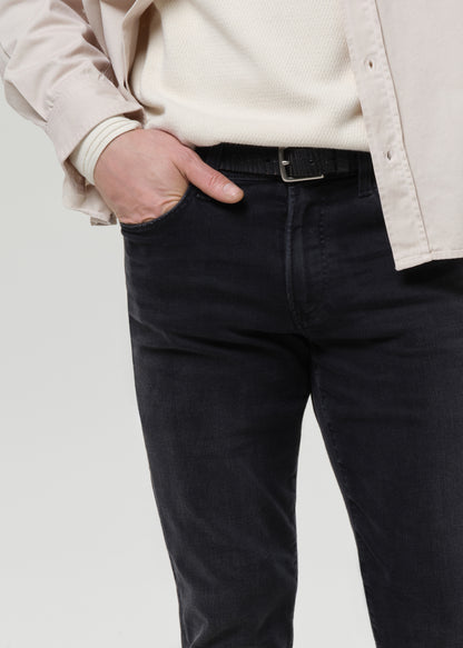 Close-up of a person wearing dark charcoal black jeans with a black belt, a cream ribbed knit top, and a light beige overshirt, with one hand in the pocket.