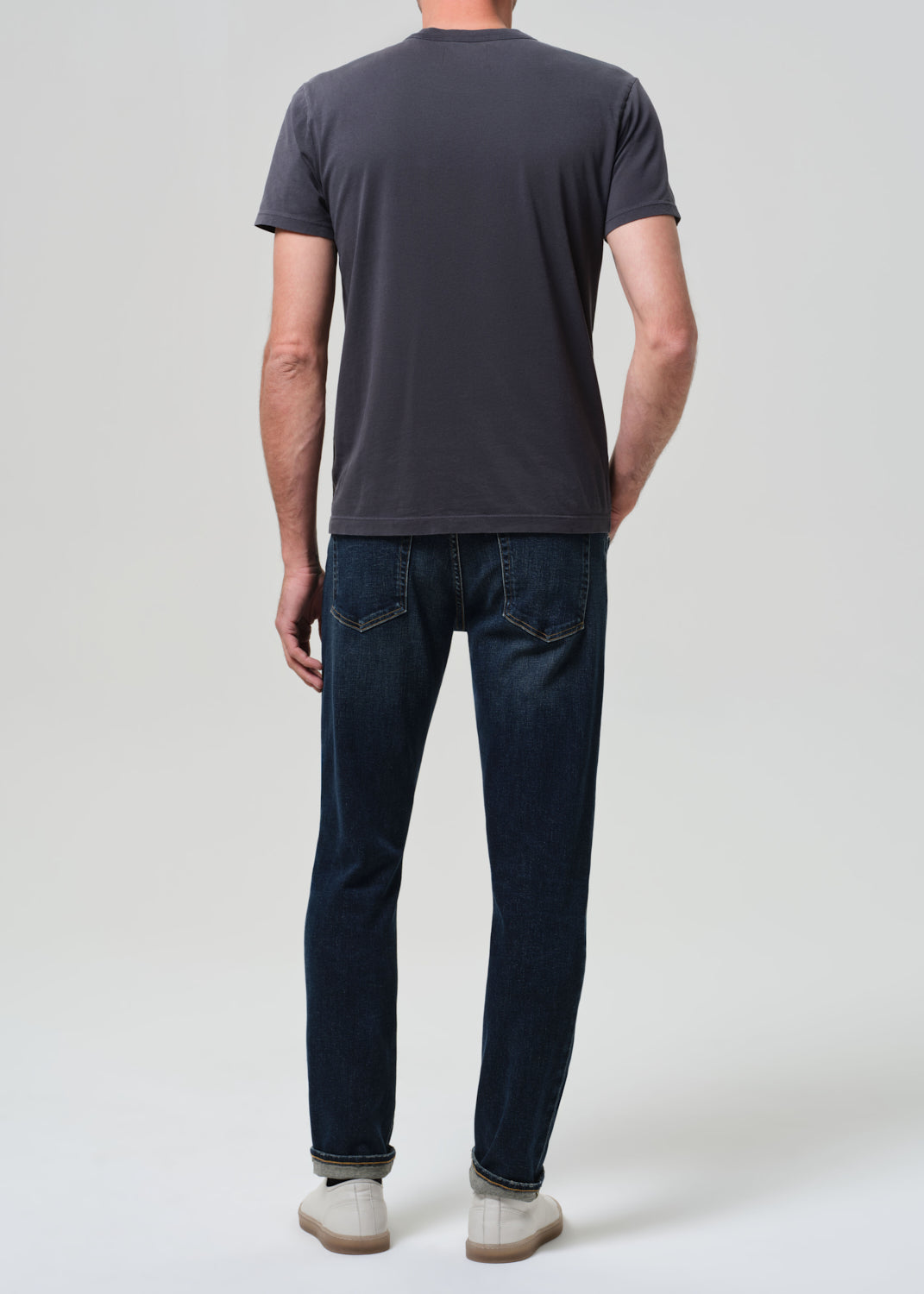 Person wearing grey tee with dark indigo jeans