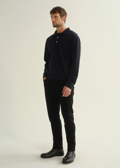 Person wearing black slim tapered jeans with a dark navy long sleeve top and black shoes, front angled view.