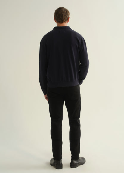 Person wearing black slim tapered jeans with a dark navy long sleeve top and black shoes, back view.