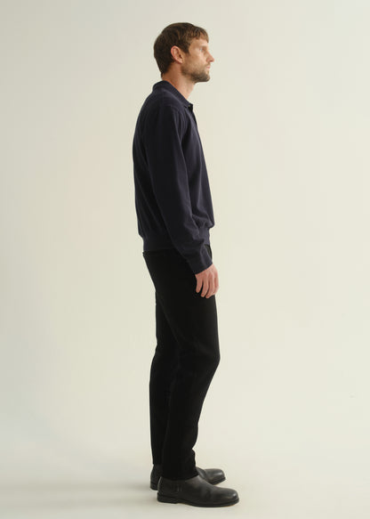 Person wearing black slim tapered jeans with a dark navy long sleeve top and black shoes, side view.