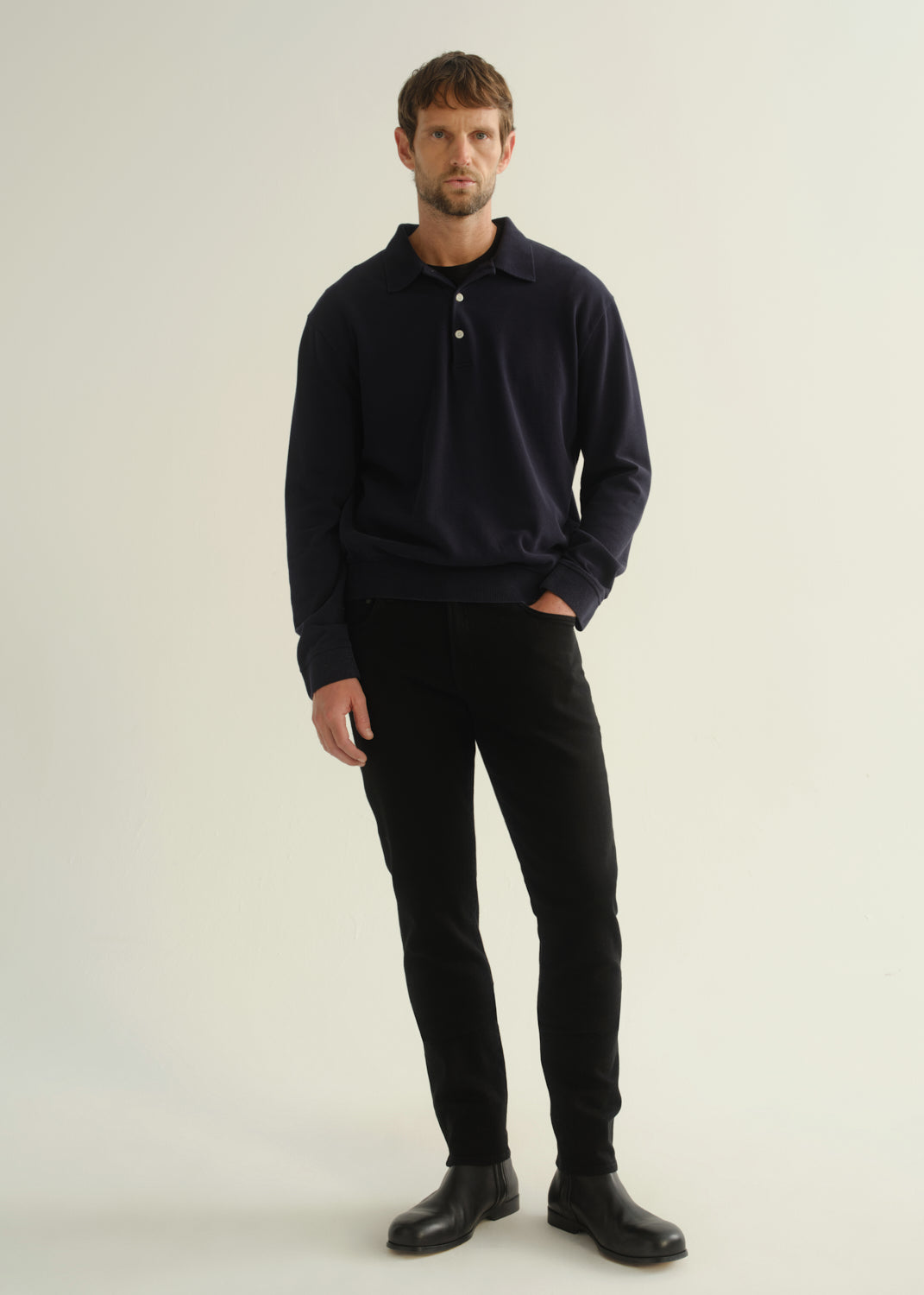Person wearing black slim tapered jeans with a dark navy long sleeve top and black shoes, front view.