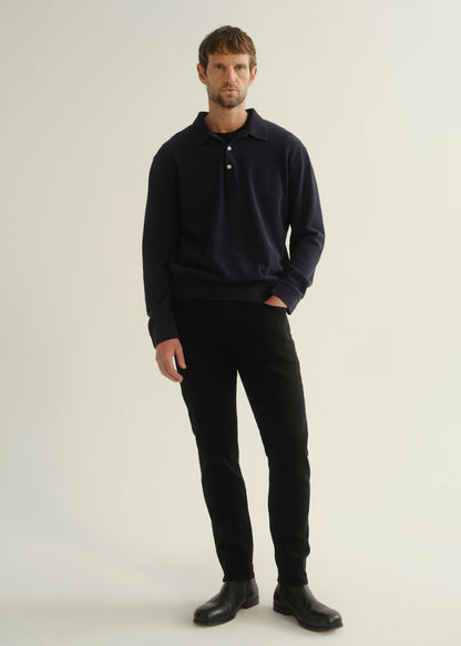 Person wearing black slim tapered jeans with a dark navy long sleeve top and black shoes, front view.