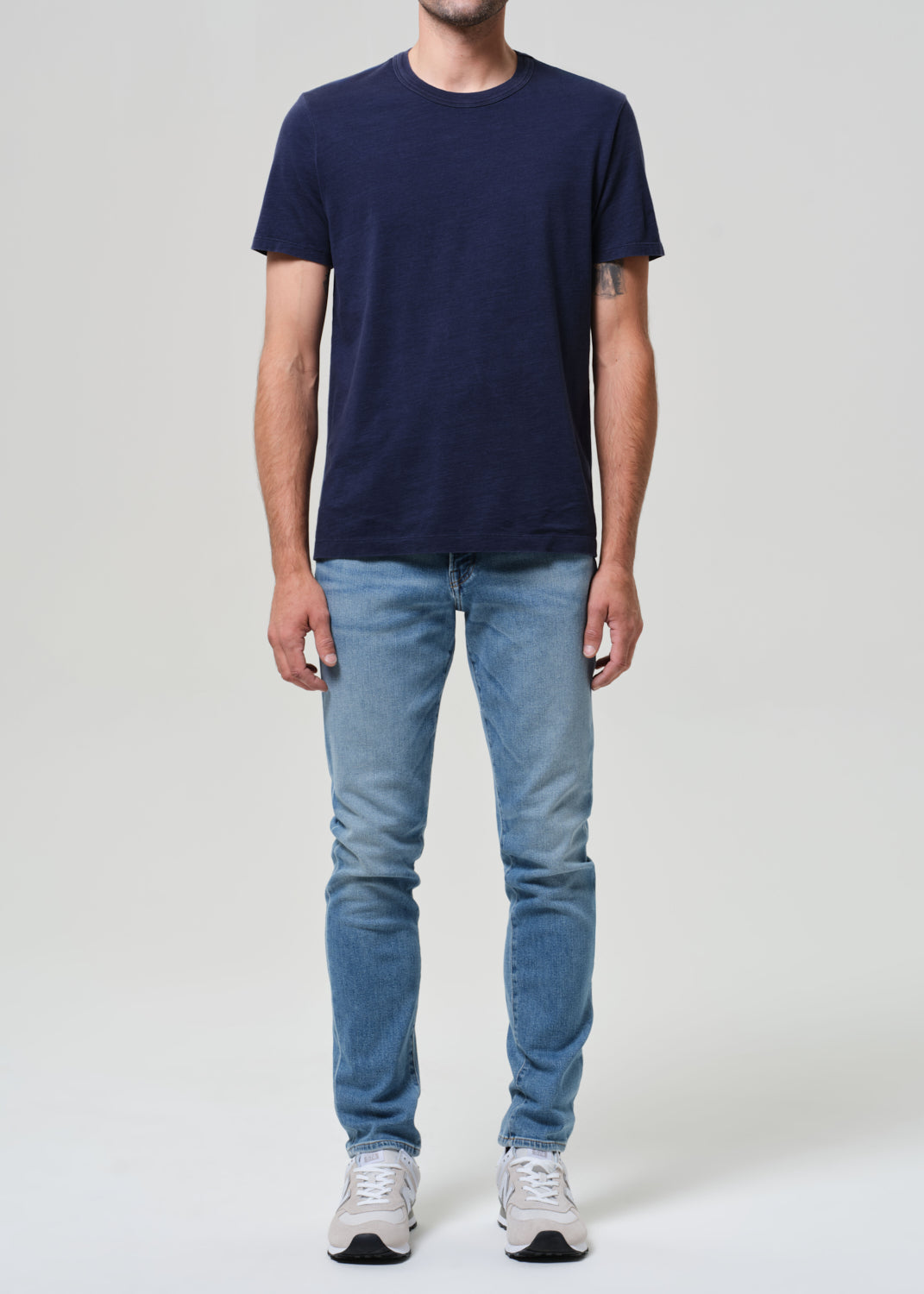 Person wearing a navy t-shirt and light blue jeans on a grey background