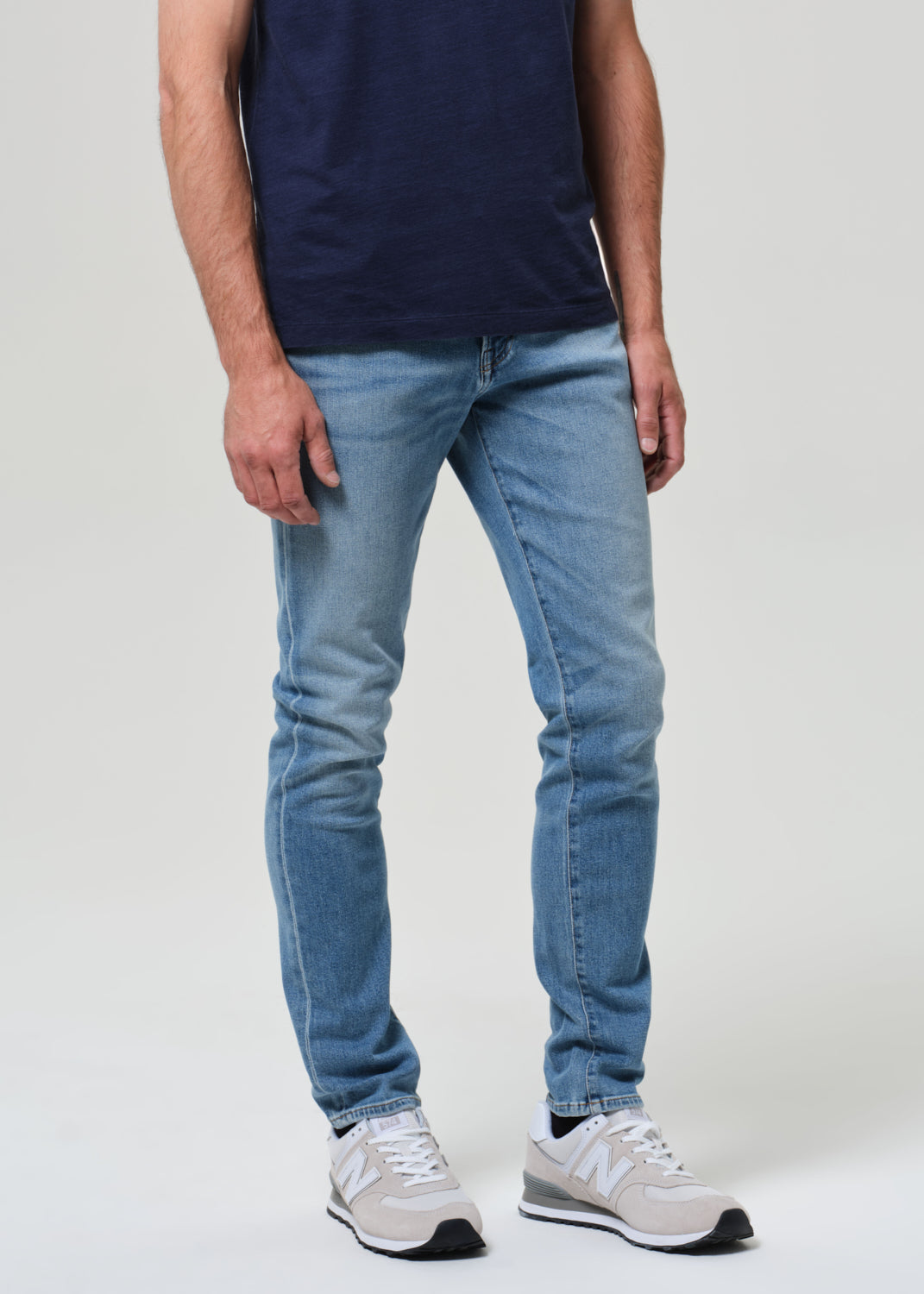 Person wearing a navy t-shirt and light blue jeans on a grey background