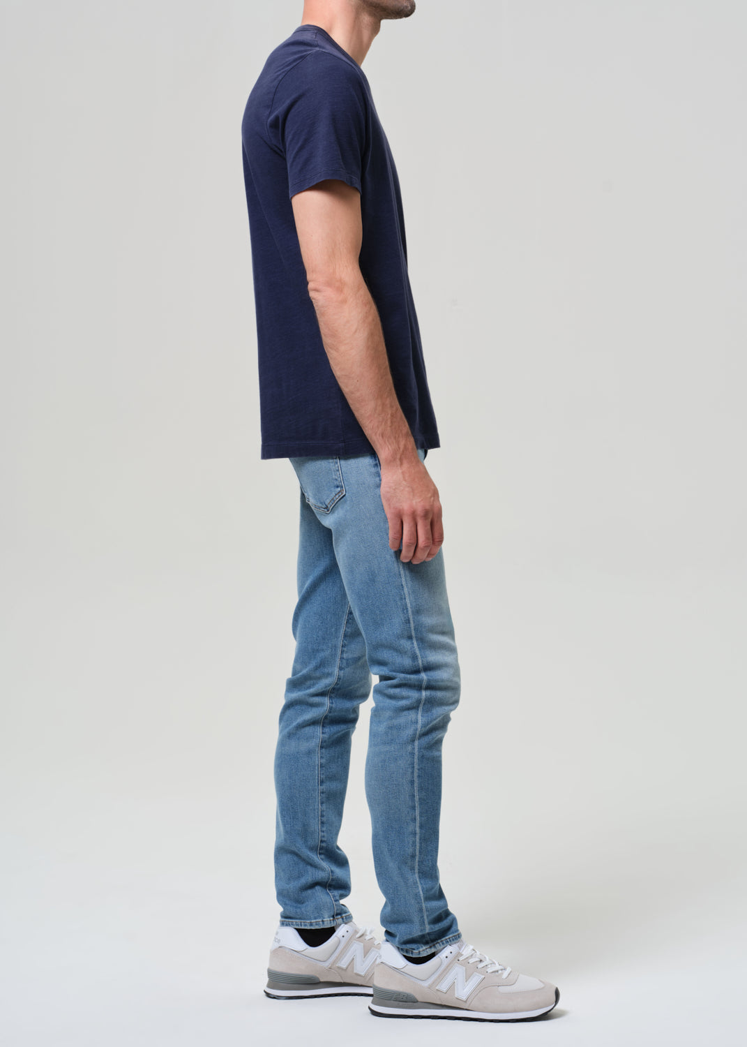 Person wearing a navy t-shirt and light blue jeans on a grey background