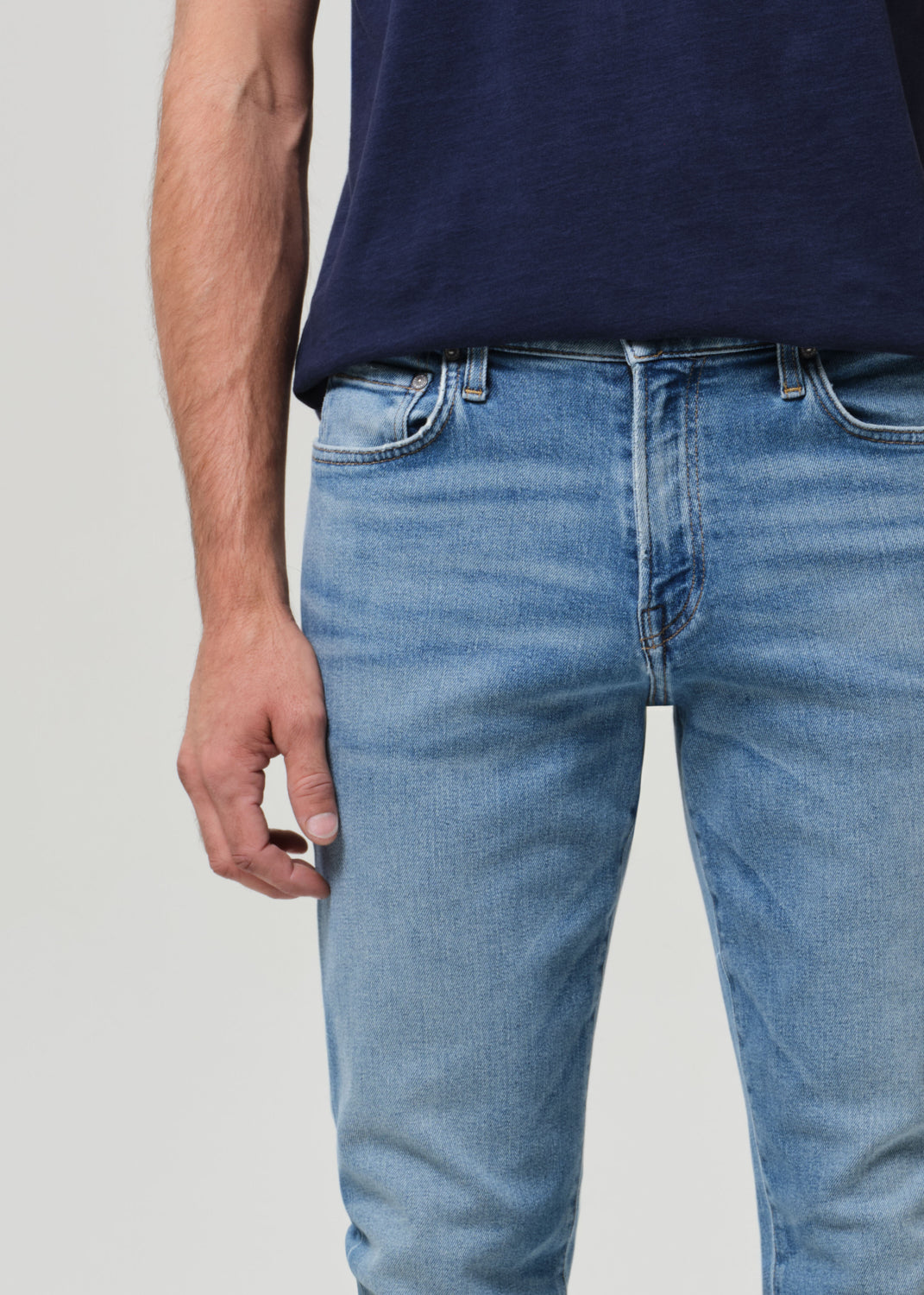Person wearing a navy t-shirt and light blue jeans on a grey background