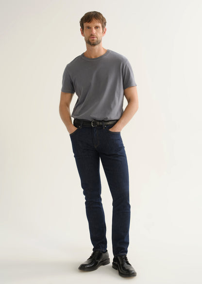 Person wearing dark indigo slim tapered jeans with a grey short sleeve crewneck t-shirt and black shoes, front view.