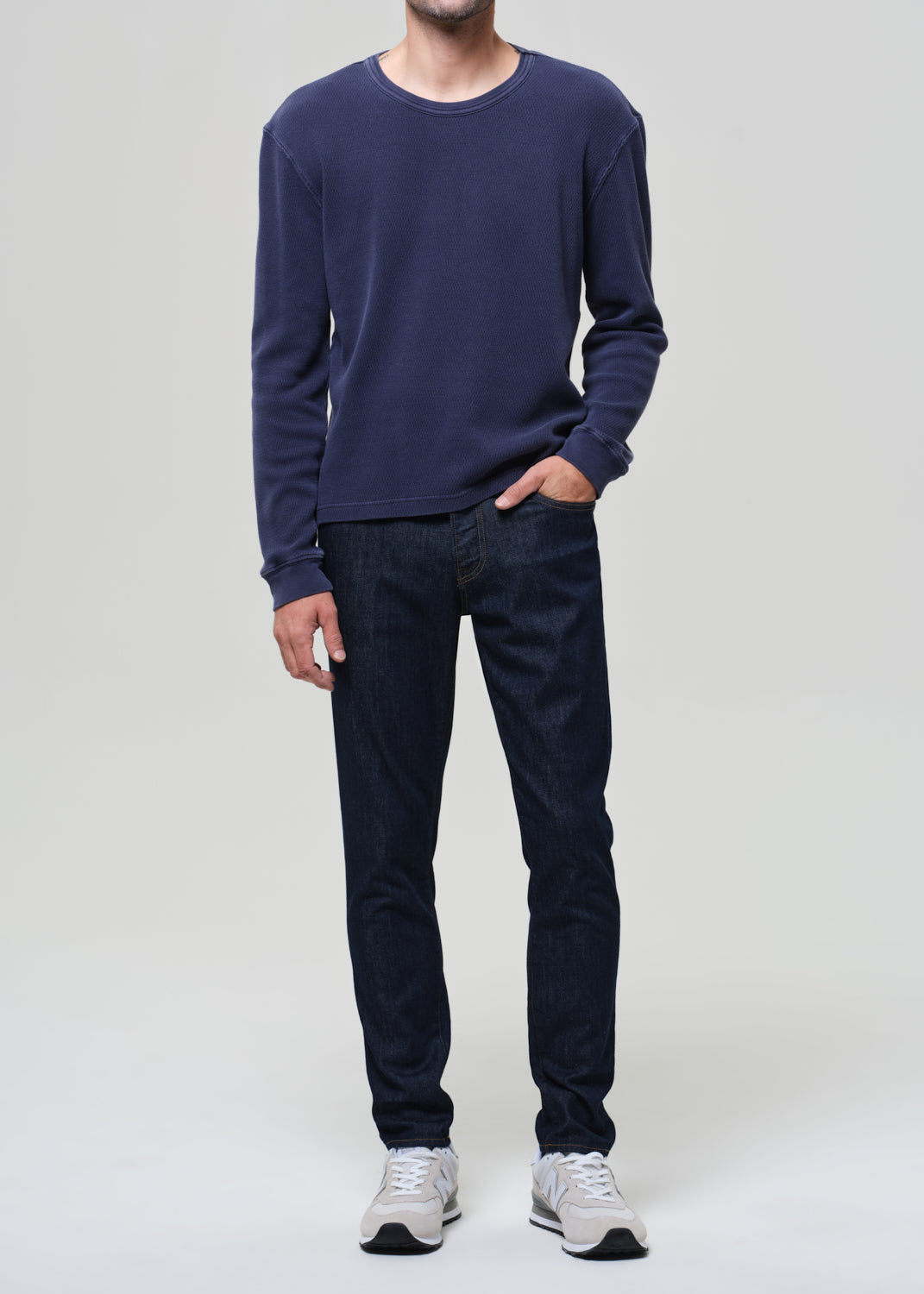 Person wearing a navy long-sleeve shirt and dark jeans on a plain background