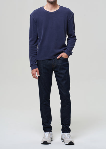 Person wearing a navy long-sleeve shirt and dark jeans on a plain background