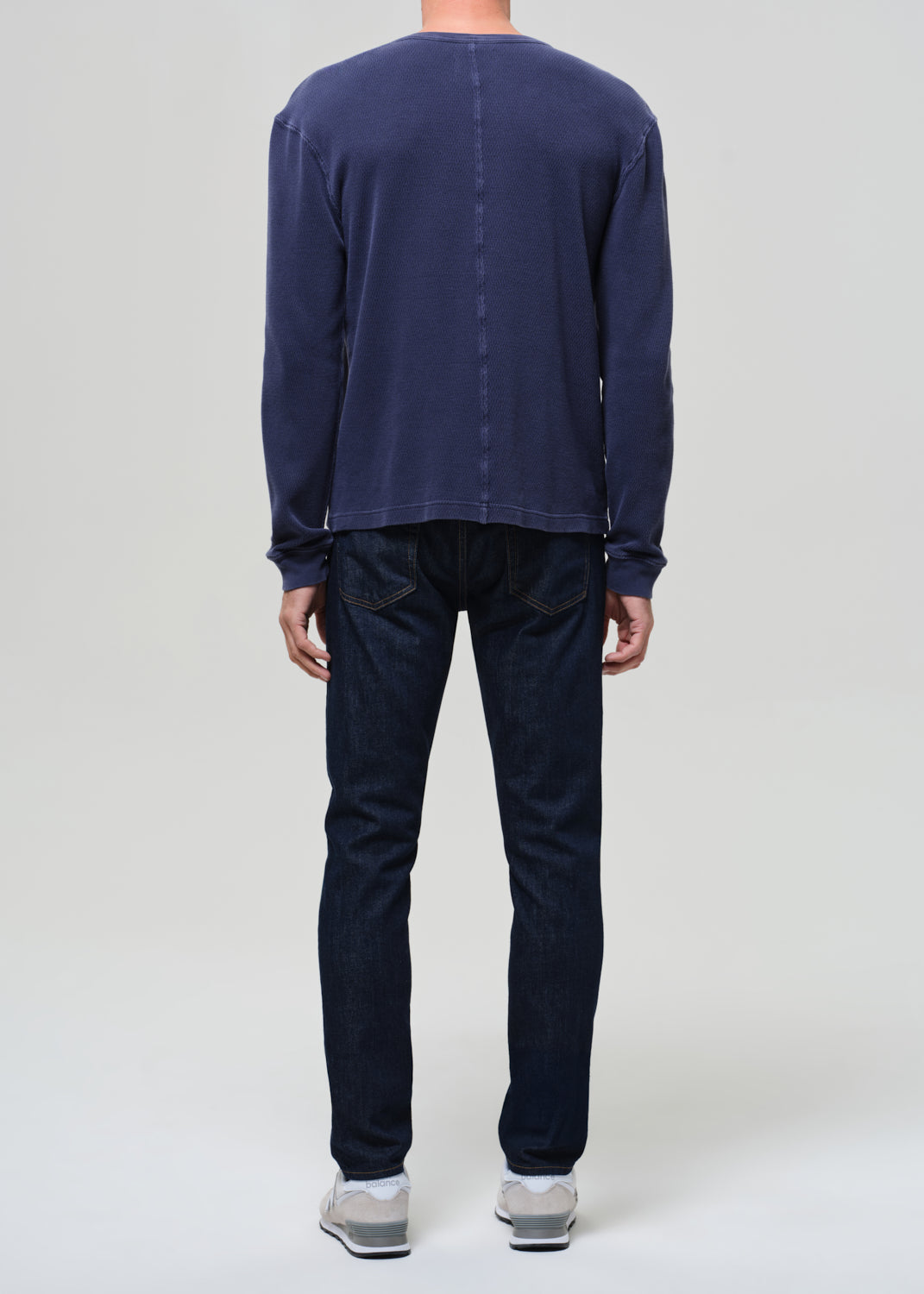 Person wearing a navy long-sleeve shirt and dark pants on a plain background