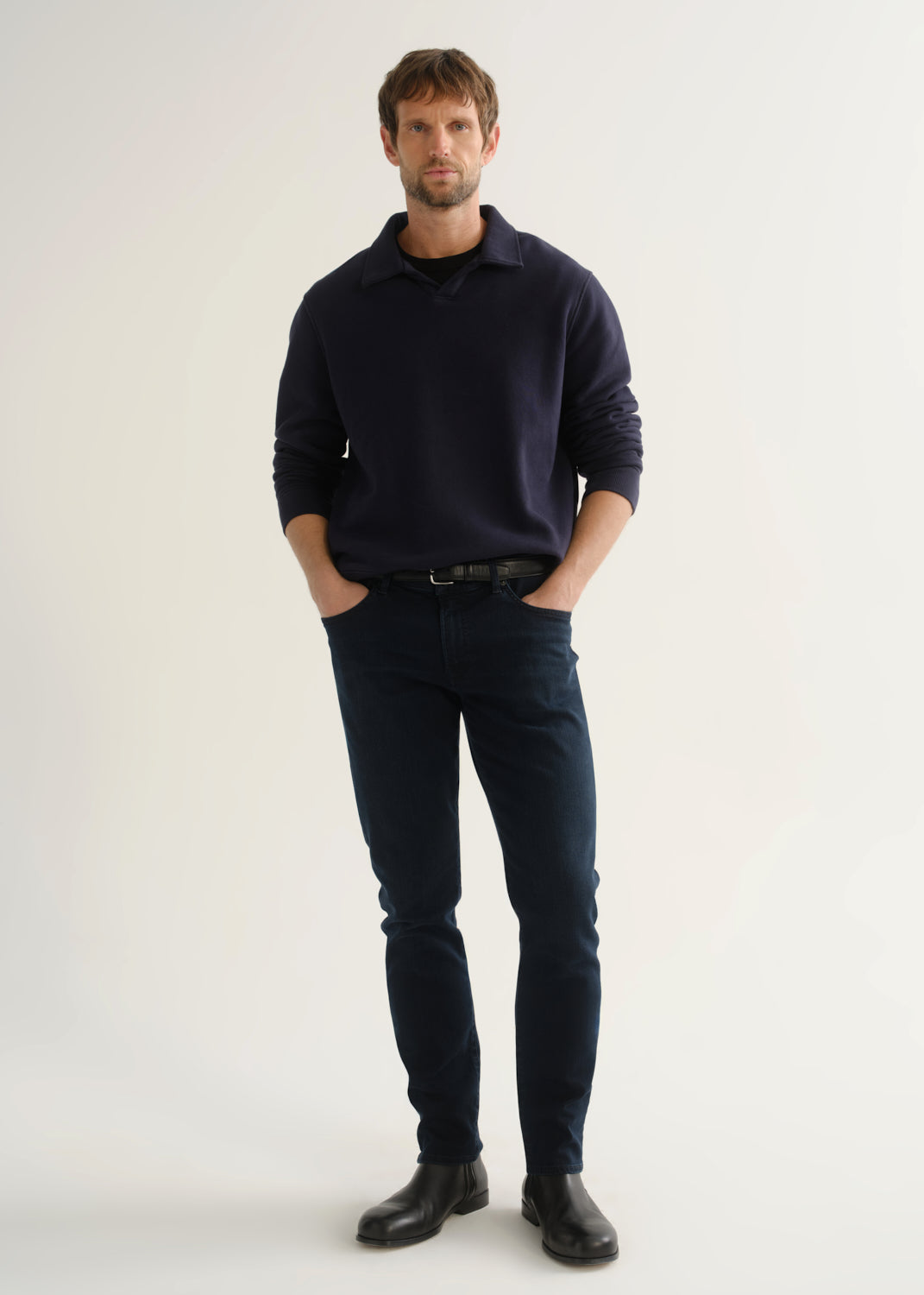 Person wearing dark navy jeans with a navy long sleeve top and black boots, front view.
