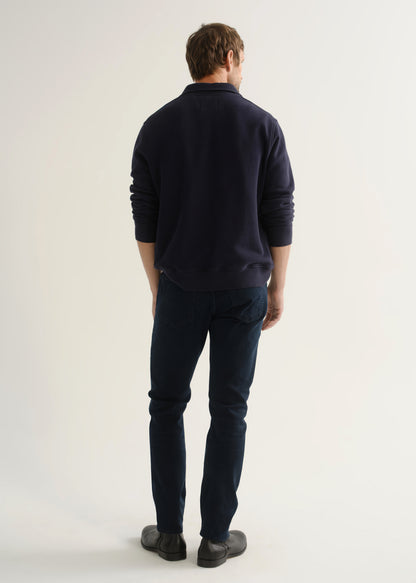 Person wearing dark navy jeans with a navy long sleeve top and black boots, back view.