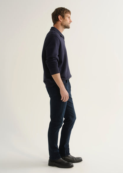 Person wearing dark navy jeans with a navy long sleeve top and black boots, side view.