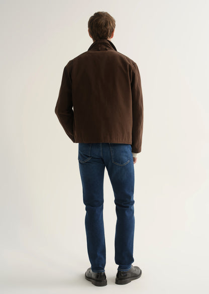 Person wearing medium blue slim tapered jeans with a brown jacket, cream sweater, and black shoes, front view.