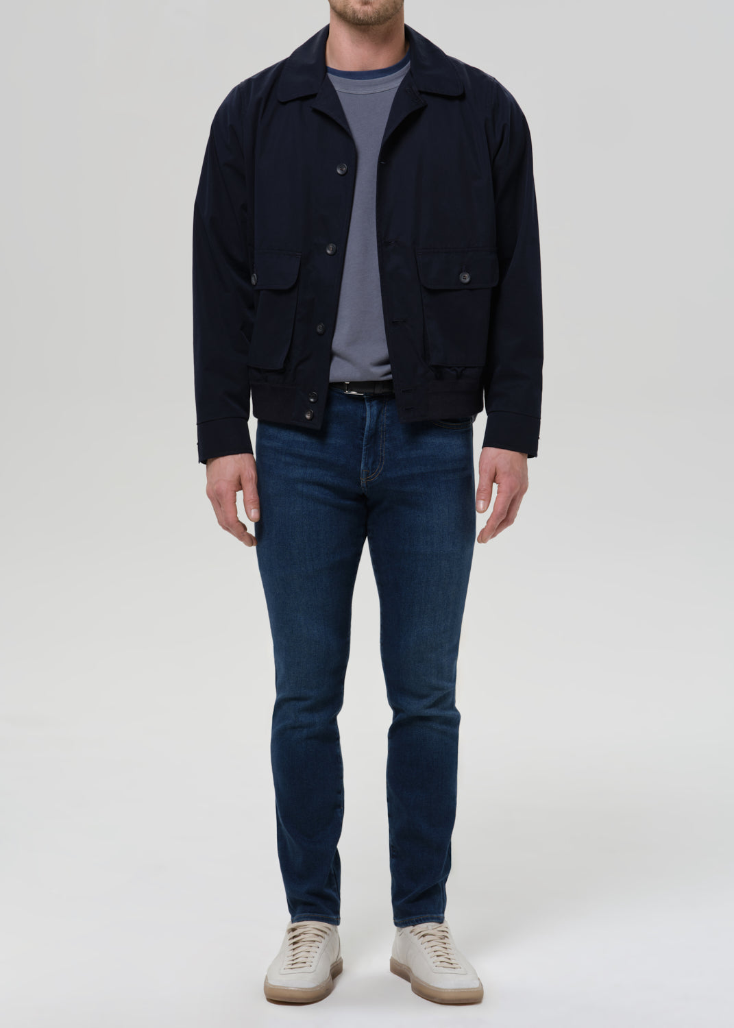 Man wearing medium blue straight leg jeans with a navy jacket and grey crewneck tee on a grey background.