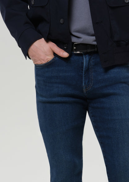 Close-up of medium blue straight leg jeans on a grey background.