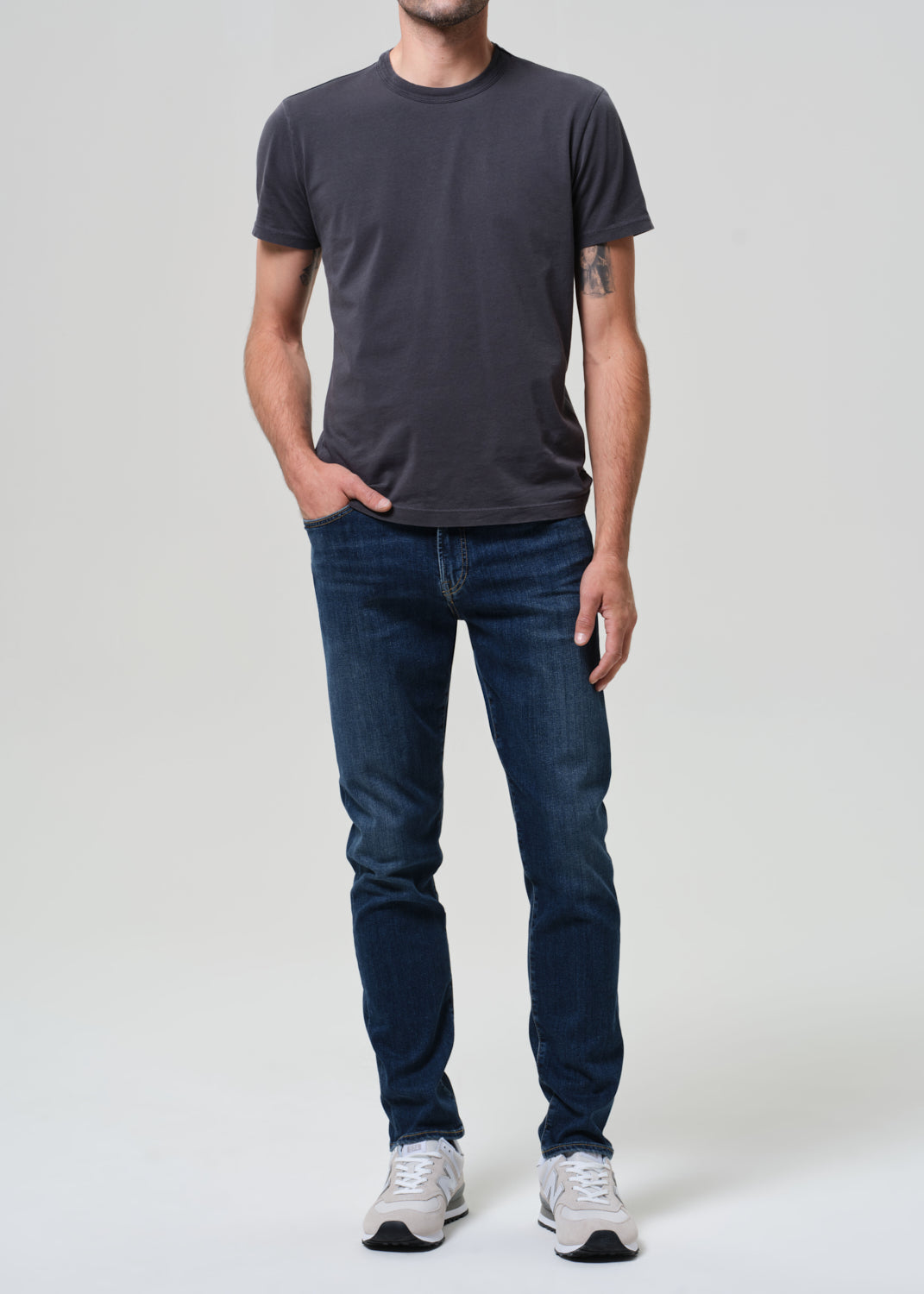 Person wearing a dark gray t-shirt and blue jeans on a white background