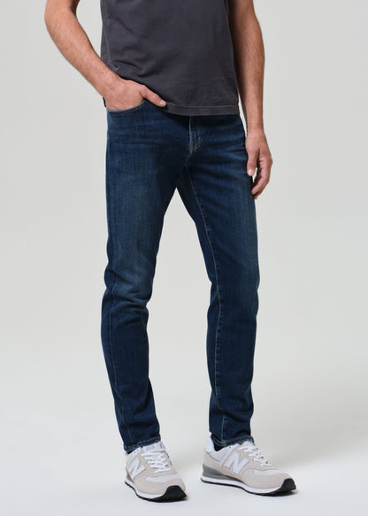 Person wearing dark blue jeans and white sneakers on a plain background