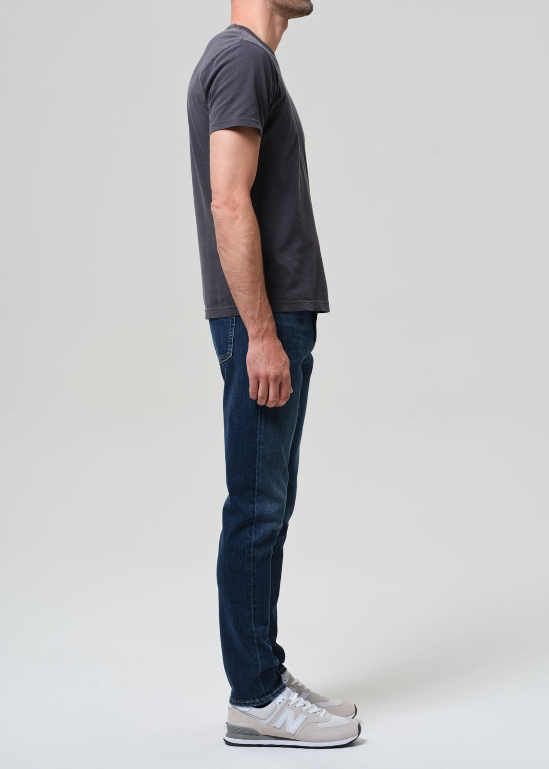 Person wearing a dark gray t-shirt and blue jeans standing against a plain white background