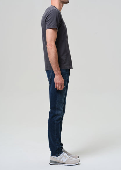 Person wearing a dark gray t-shirt and blue jeans standing against a plain white background