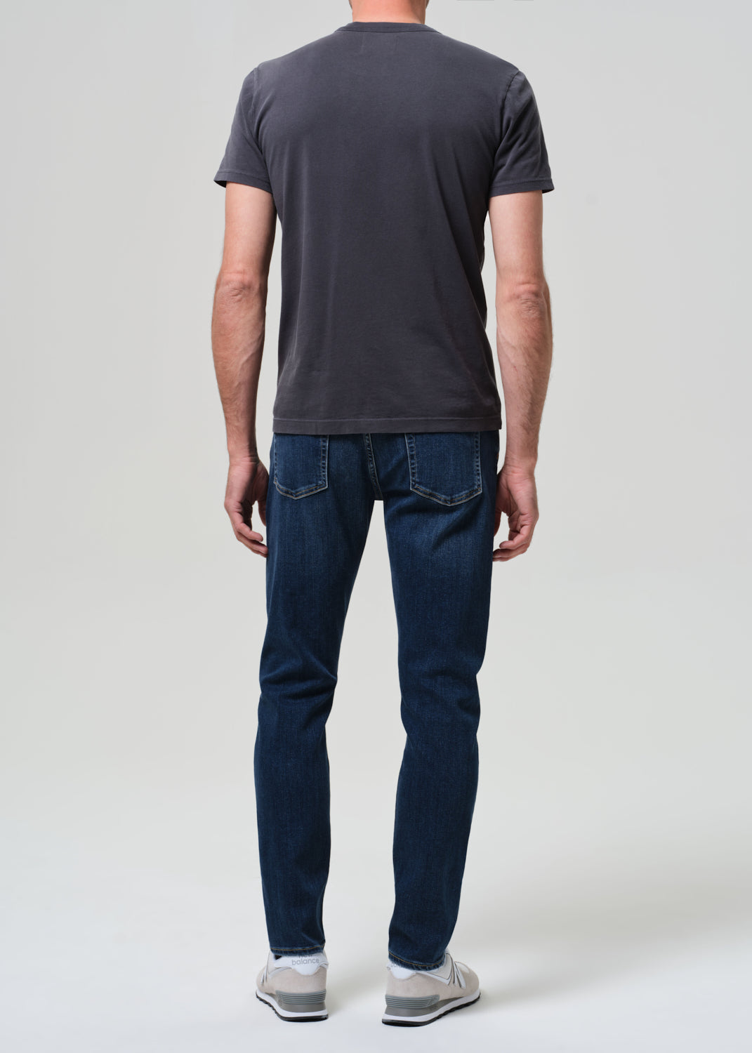 Person wearing a dark gray t-shirt and blue jeans on a white background