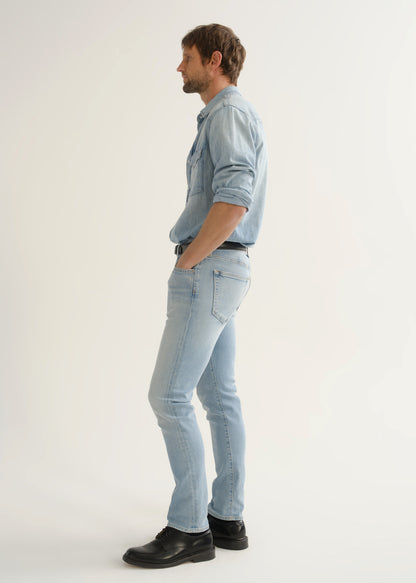 Person wearing light wash blue slim tapered jeans with a light blue denim shirt, white tee, black belt, and black shoes, front angled view.