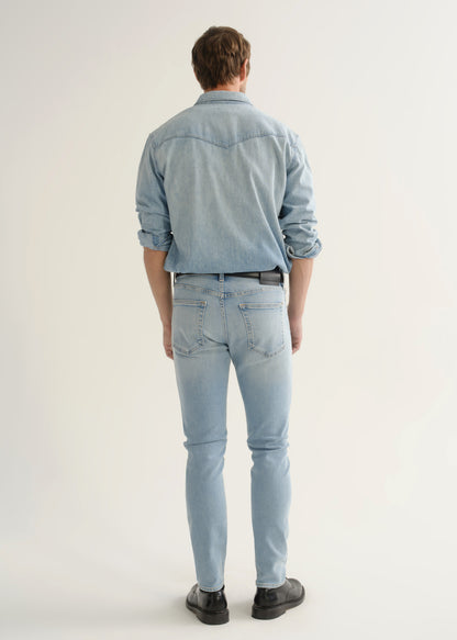 Person wearing light wash blue slim tapered jeans with a light blue denim shirt, white tee, black belt, and black shoes, front view.