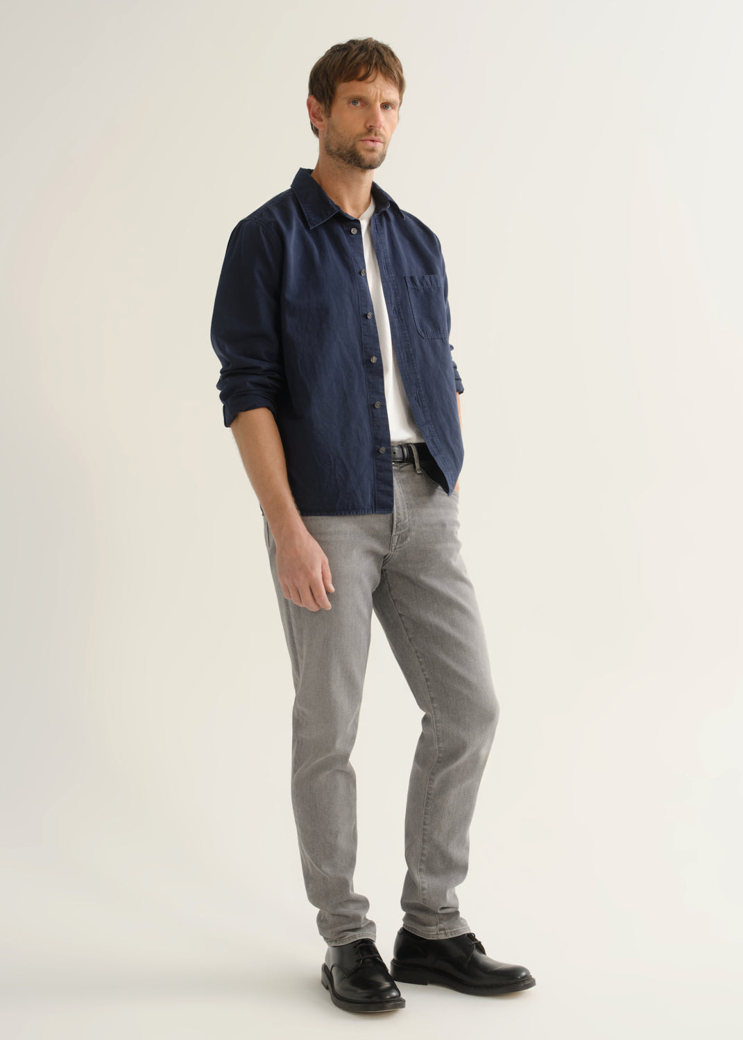 Person wearing light grey slim tapered jeans with a navy long sleeve button-up shirt and black shoes, back view.