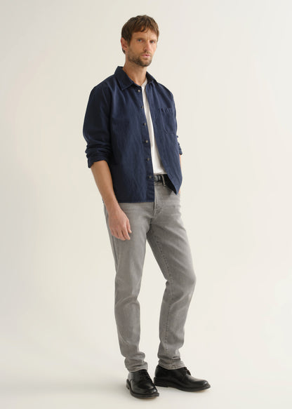 Person wearing light grey slim tapered jeans with a navy long sleeve button-up shirt and black shoes, back view.