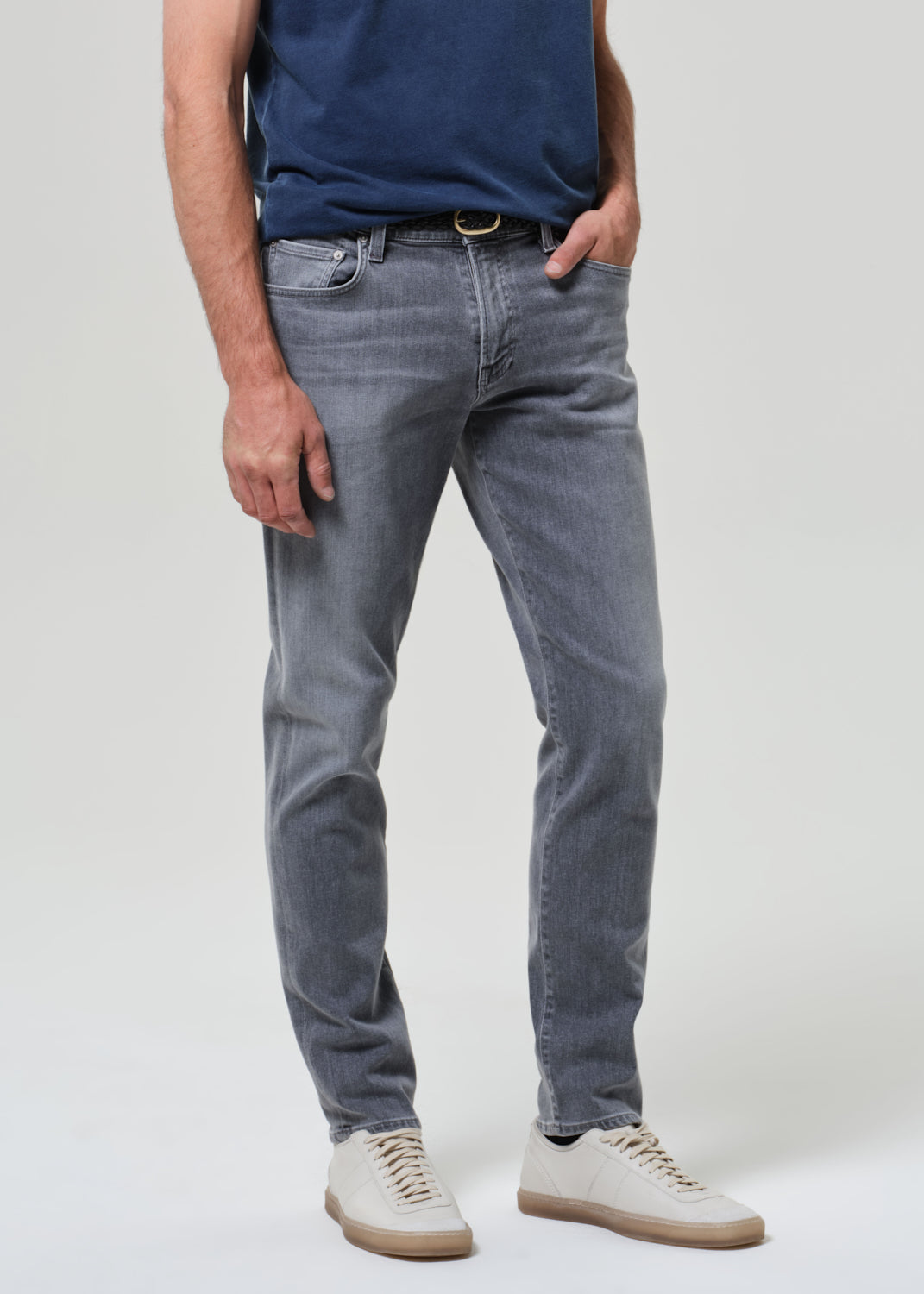 Person wearing a navy t-shirt and gray jeans on a grey background