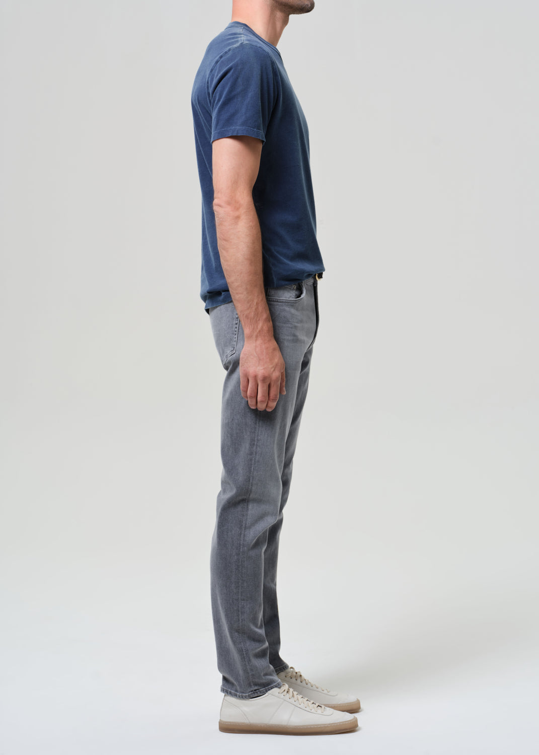 Person wearing a navy t-shirt and gray jeans on a grey background
