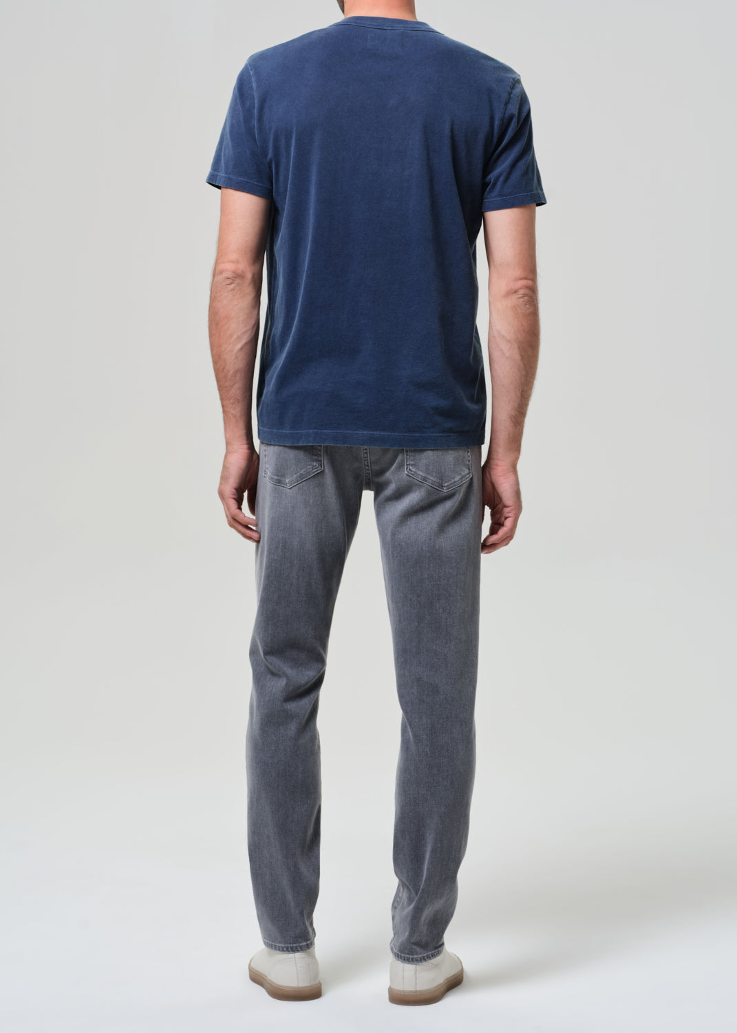 Person wearing a navy t-shirt and gray jeans on a grey background