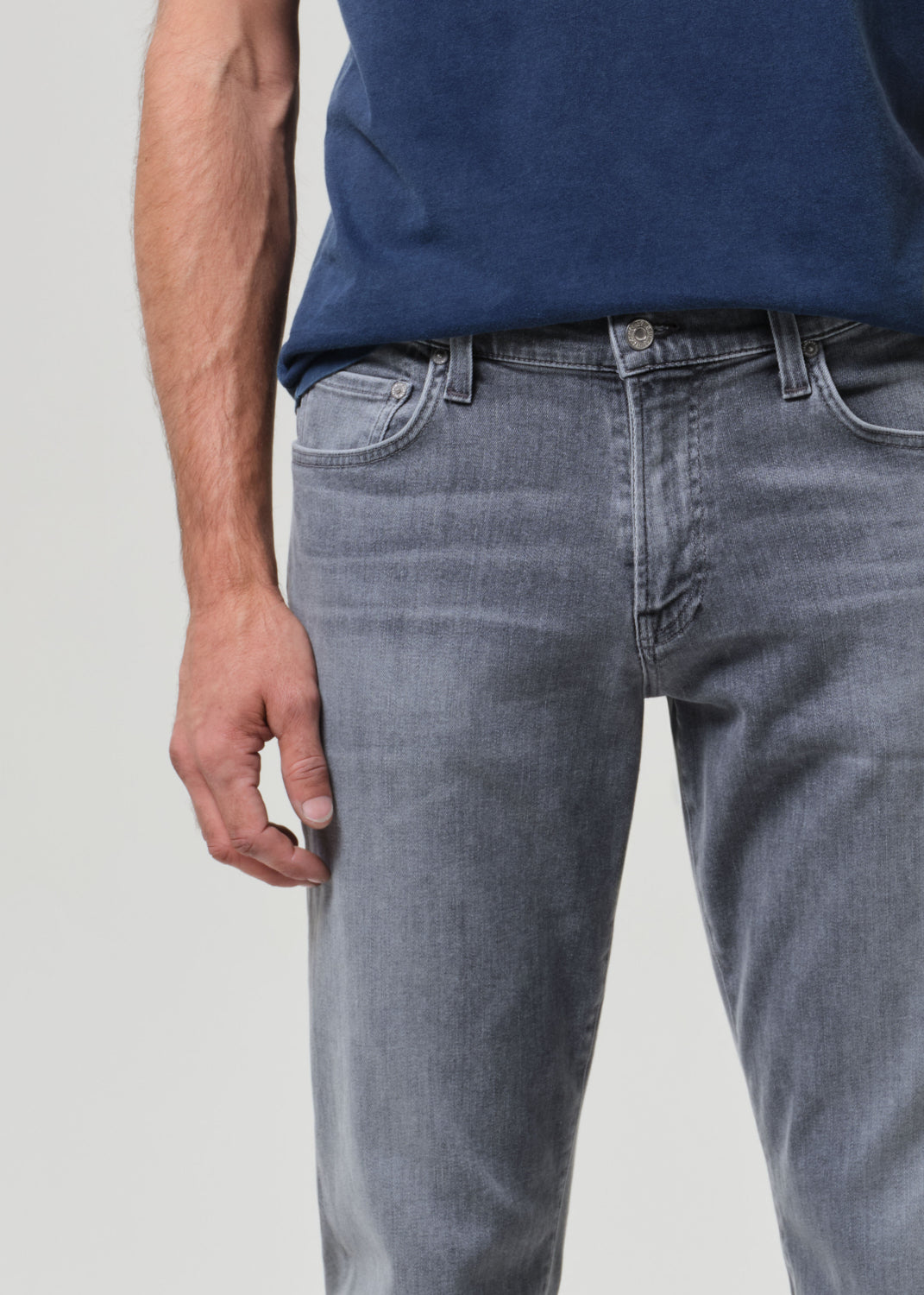 Person wearing a navy t-shirt and gray jeans on a grey background