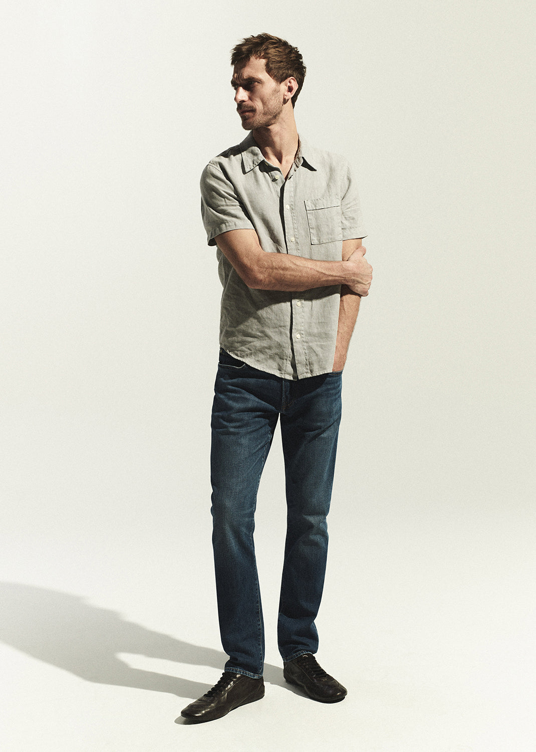Man wearing a light grey shirt and dark blue jeans against a white background
