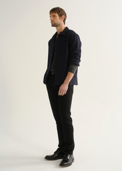 Person wearing black slim tapered jeans with a dark navy button-up overshirt, charcoal grey shirt, and black shoes, front angled view.