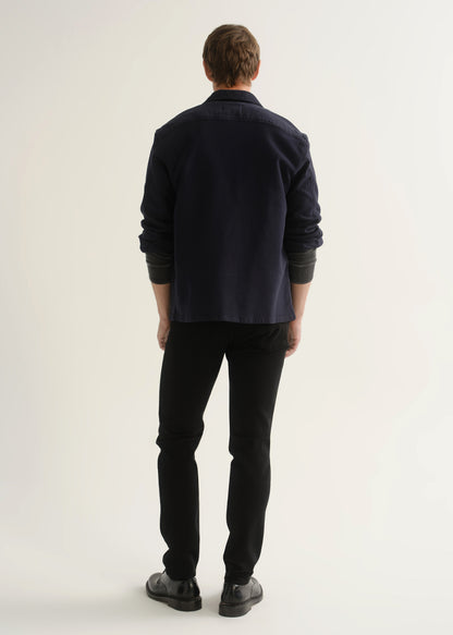 Person wearing black slim tapered jeans with a dark navy button-up overshirt, charcoal grey shirt, and black shoes, back view.