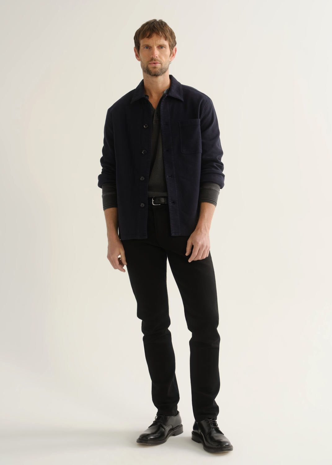 Person wearing black slim tapered jeans with a dark navy button-up overshirt, charcoal grey shirt, and black shoes, front view.
