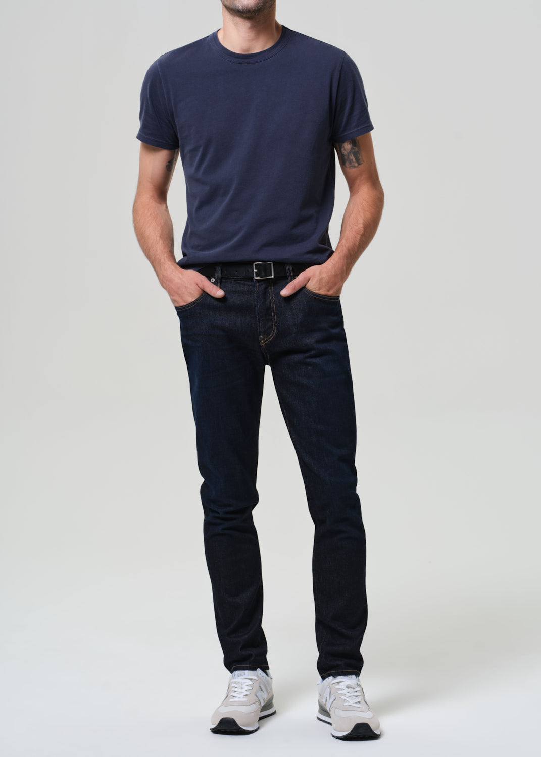 Man wearing a navy t-shirt and dark wash jeans against a grey background