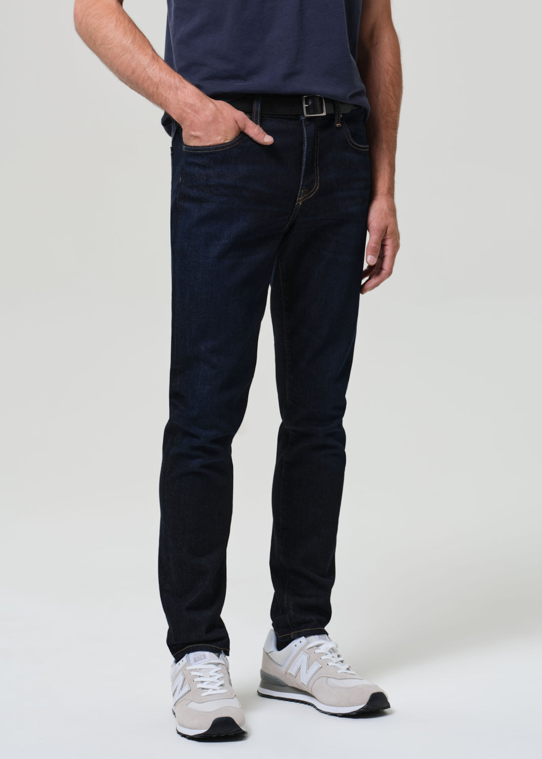 Man wearing a navy t-shirt and dark wash jeans against a grey background