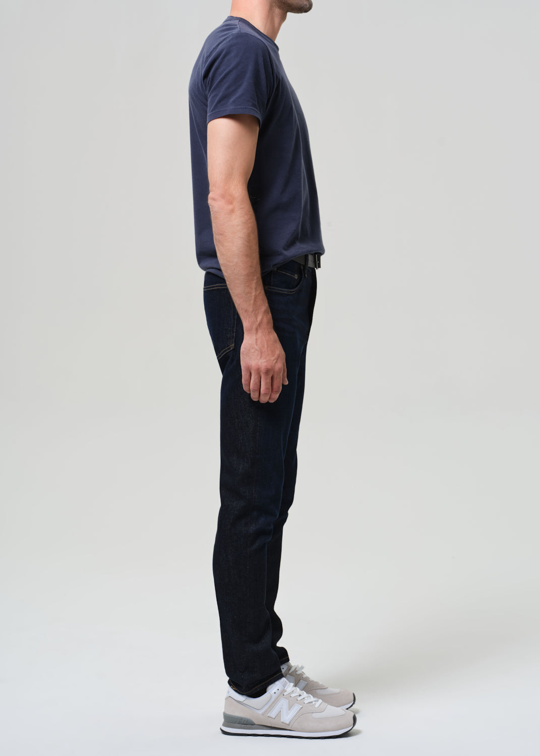 Man wearing a navy t-shirt and dark wash jeans against a grey background