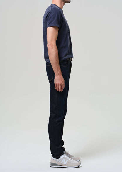 Man wearing a navy t-shirt and dark wash jeans against a grey background