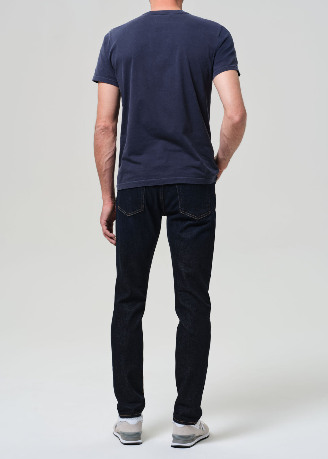 Man wearing a navy t-shirt and dark wash jeans against a grey background